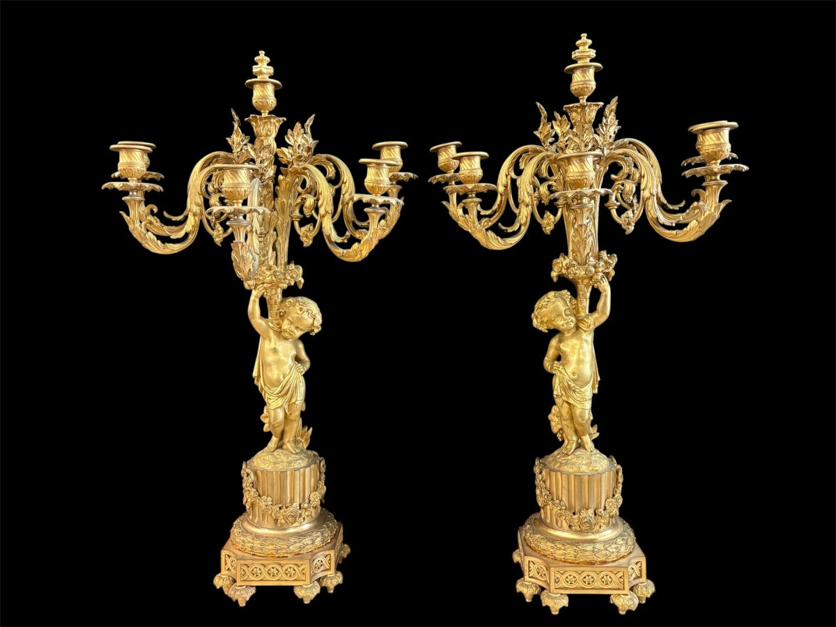 Large gilt bronze clock set. Paris, 19th century. A beautiful large clock with four cherubs and very fine gilt bronze decorations, as well as two candlesticks representing two large cherubs carrying a torch with six candlesticks.