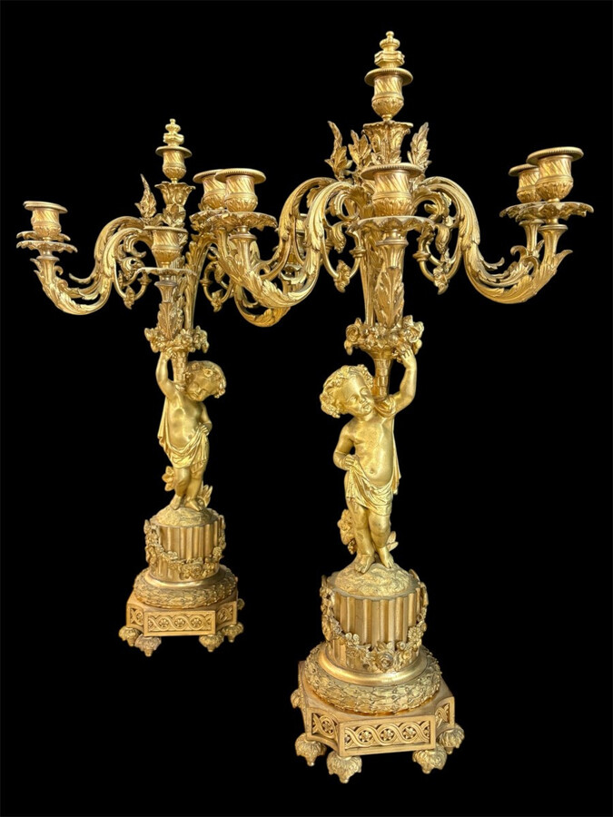 Large gilt bronze clock set. Paris, 19th century. A beautiful large clock with four cherubs and very fine gilt bronze decorations, as well as two candlesticks representing two large cherubs carrying a torch with six candlesticks.