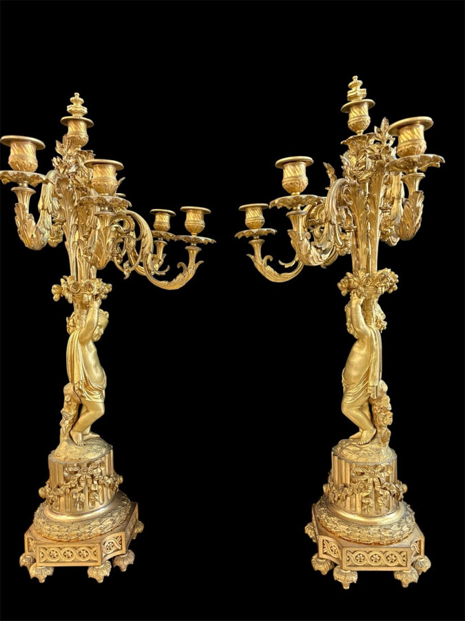 Large gilt bronze clock set. Paris, 19th century. A beautiful large clock with four cherubs and very fine gilt bronze decorations, as well as two candlesticks representing two large cherubs carrying a torch with six candlesticks.