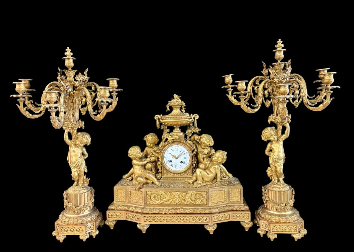 Large gilt bronze clock set. Paris, 19th century. A beautiful large clock with four cherubs and very fine gilt bronze decorations, as well as two candlesticks representing two large cherubs carrying a torch with six candlesticks.