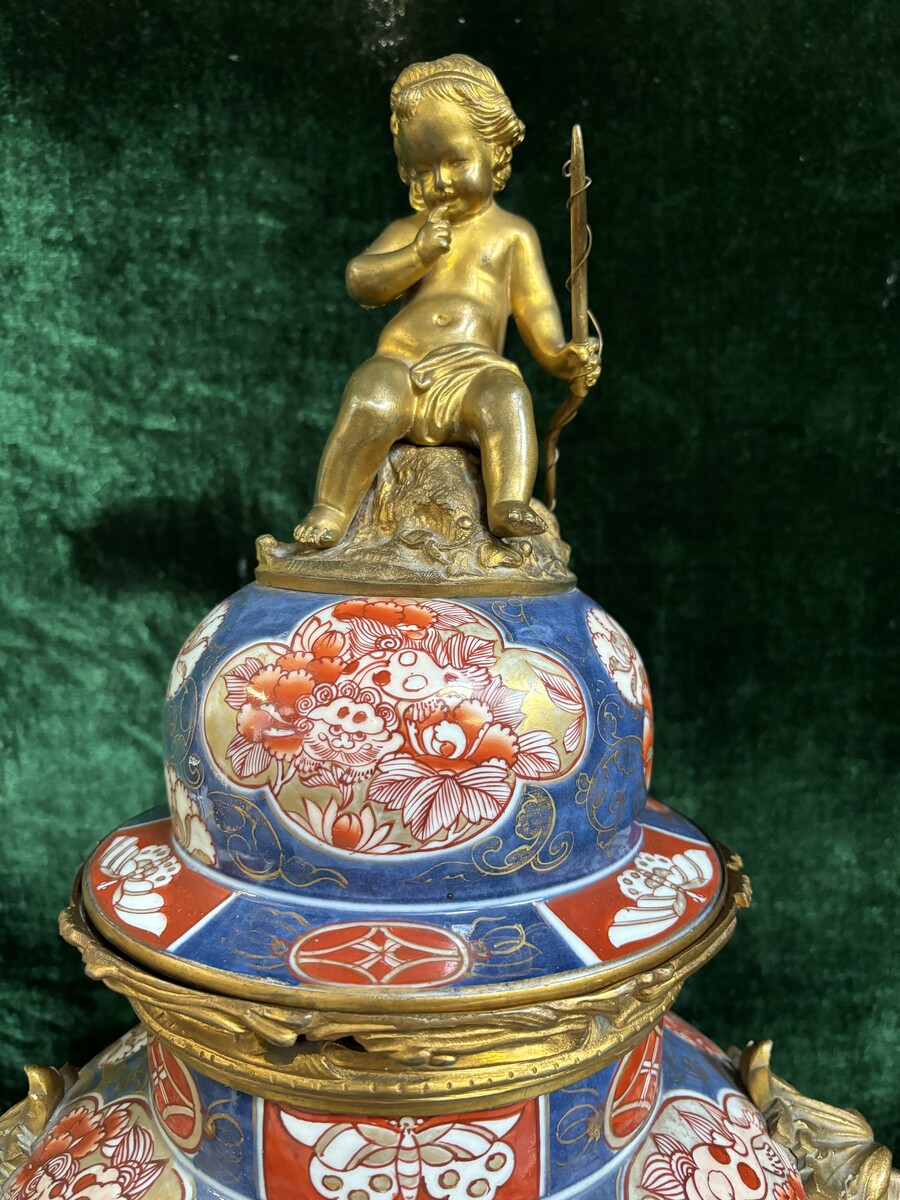 Large mantelpiece in porcelain and gilt bronze 19th century. Fireplace garniture comprising a large lidded vase/clock with 2 lidded vases in porcelain decorated with gilt bronze ornaments , lion heads and music-making putti. Key and pendulum present 