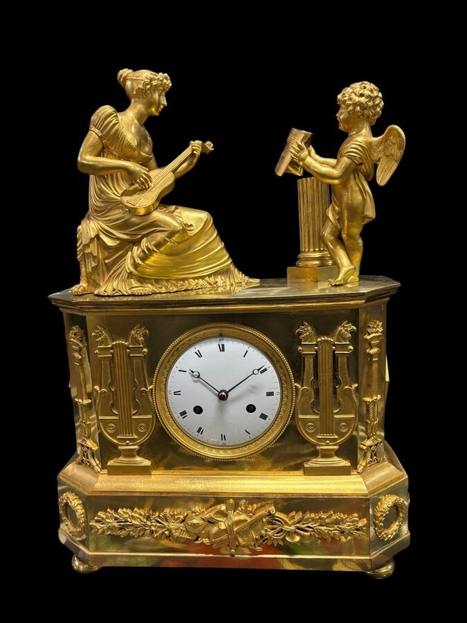 Nice Empire period clock in matt and bright gilt bronze depicting a lady playing guitar with an angel. In very good condition, the movement has not been checked. The balance wheel is present. Dimensions: Width: 31.5 cm Height: 43 cm Depth : 13 cm