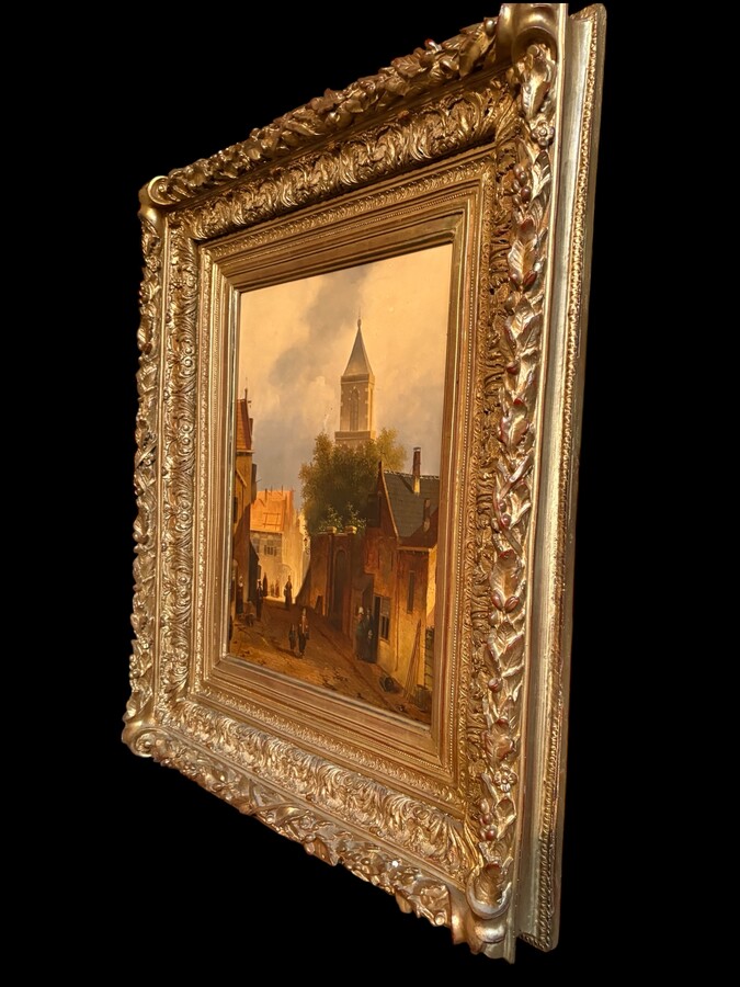 Painting ‘View of an Old Dutch Town’ oil on panel, 19th century Decorative painting in a large gilded frame depicting an old town, a street with old houses, a church, a gate with a municipal garden and various figures. 