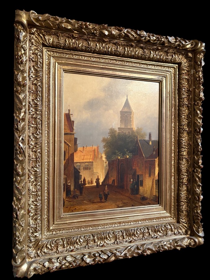 Painting ‘View of an Old Dutch Town’ oil on panel, 19th century Decorative painting in a large gilded frame depicting an old town, a street with old houses, a church, a gate with a municipal garden and various figures. 