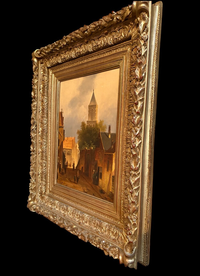 Painting ‘View of an Old Dutch Town’ oil on panel, 19th century Decorative painting in a large gilded frame depicting an old town, a street with old houses, a church, a gate with a municipal garden and various figures.
