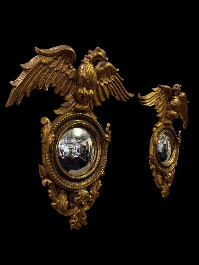 Pair of decorative ‘Eagles’ mirrors in gilded wood, late 19th century. Gilded wooden frame decorated with scrolls, paintings, a large gilded eagle and a convex mirror. Diameter of the curved mirror: 25 cm. 