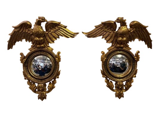 Pair of decorative ‘Eagles’ mirrors in gilded wood, late 19th century. Gilded wooden frame decorated with scrolls, paintings, a large gilded eagle and a convex mirror. Diameter of the curved mirror: 25 cm. 