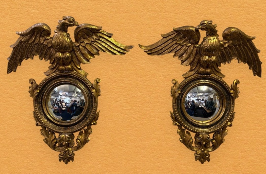 Pair of decorative ‘Eagles’ mirrors in gilded wood, late 19th century. Gilded wooden frame decorated with scrolls, paintings, a large gilded eagle and a convex mirror. Diameter of the curved mirror: 25 cm.