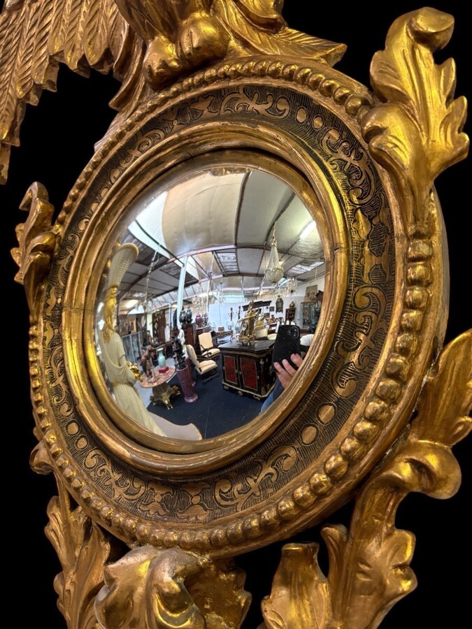 Pair of decorative ‘Eagles’ mirrors in gilded wood, late 19th century. Gilded wooden frame decorated with scrolls, paintings, a large gilded eagle and a convex mirror. Diameter of the curved mirror: 25 cm.
