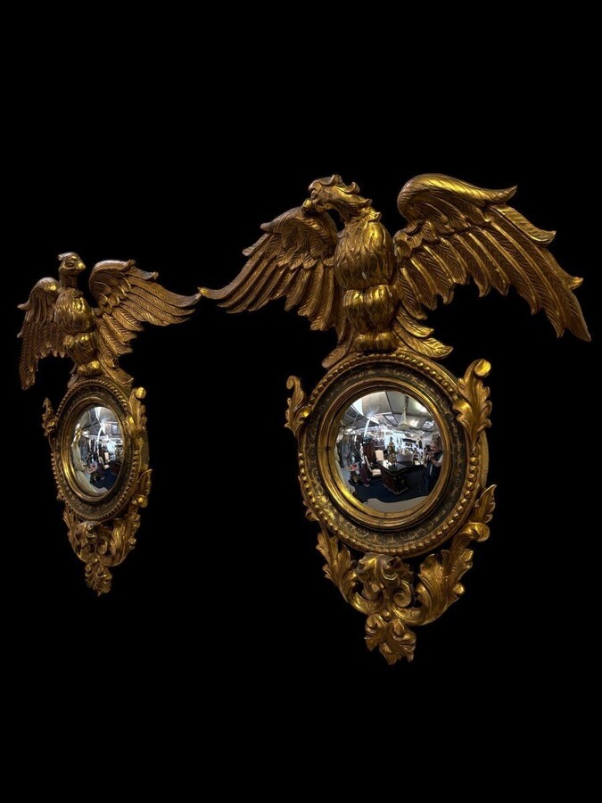 Pair of decorative ‘Eagles’ mirrors in gilded wood, late 19th century. Gilded wooden frame decorated with scrolls, paintings, a large gilded eagle and a convex mirror. Diameter of the curved mirror: 25 cm.