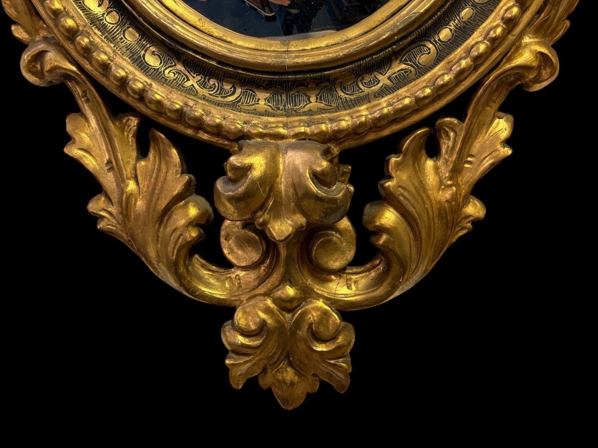 Pair of decorative ‘Eagles’ mirrors in gilded wood, late 19th century. Gilded wooden frame decorated with scrolls, paintings, a large gilded eagle and a convex mirror. Diameter of the curved mirror: 25 cm.