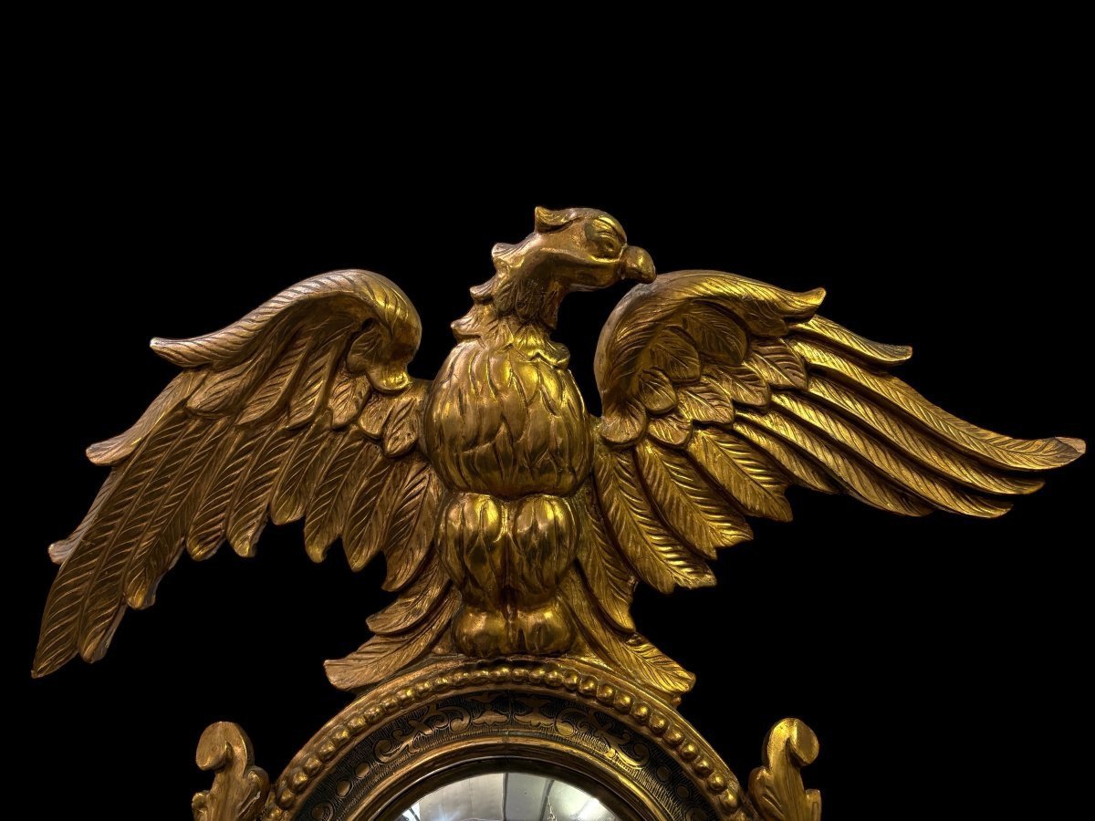 Pair of decorative ‘Eagles’ mirrors in gilded wood, late 19th century. Gilded wooden frame decorated with scrolls, paintings, a large gilded eagle and a convex mirror. Diameter of the curved mirror: 25 cm.