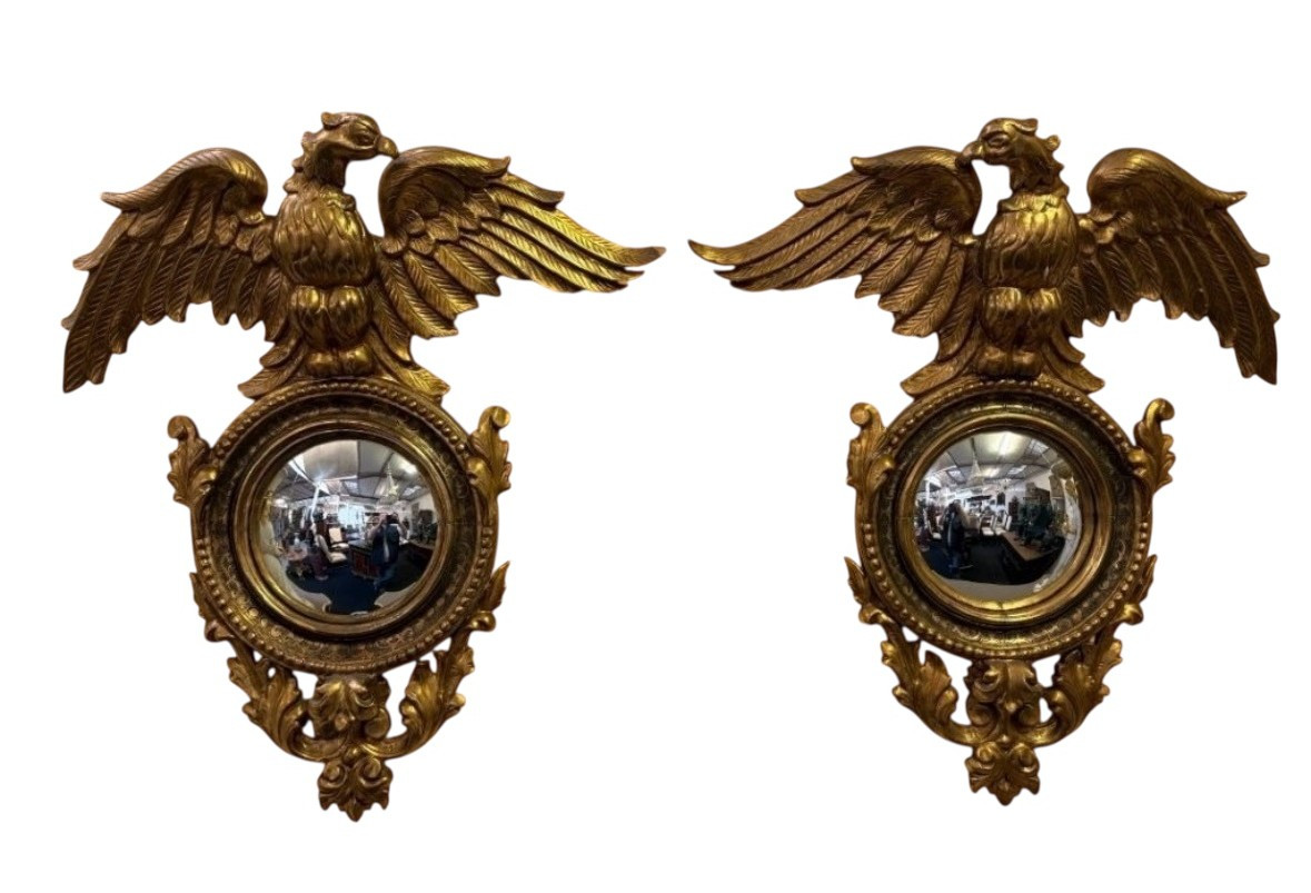 Pair of decorative ‘Eagles’ mirrors in gilded wood, late 19th century. Gilded wooden frame decorated with scrolls, paintings, a large gilded eagle and a convex mirror. Diameter of the curved mirror: 25 cm.