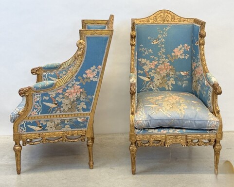 Pair of giltwood bergères in the Louis Seize style 1900 Decorative bergères adorned with garlands and carved ornaments and upholstered in a beautiful blue fabric with bird and flower motifs. The seat of one of the armchairs needs restoring!