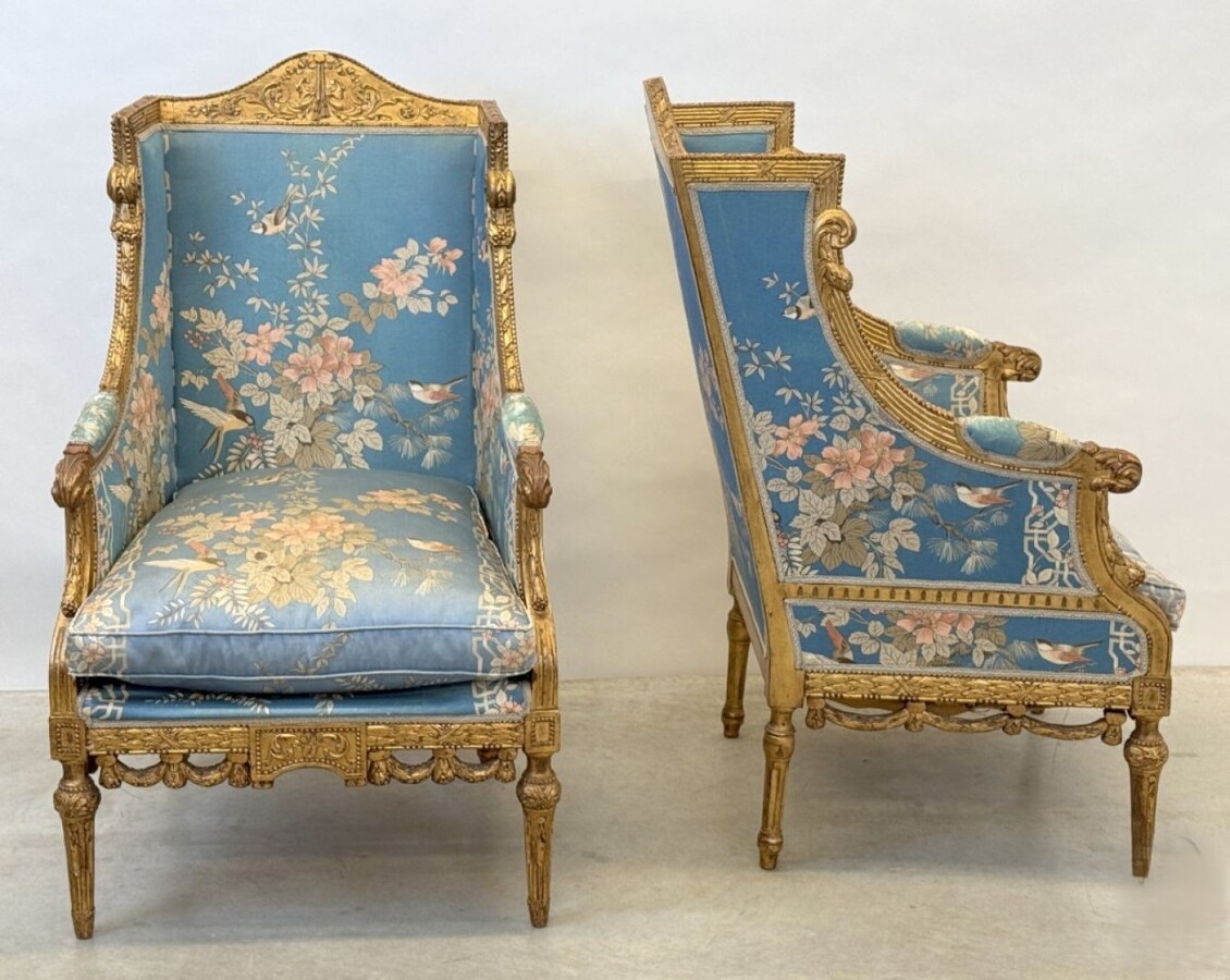 Pair of giltwood bergères in the Louis Seize style 1900 Decorative bergères adorned with garlands and carved ornaments and upholstered in a beautiful blue fabric with bird and flower motifs. The seat of one of the armchairs needs restoring!