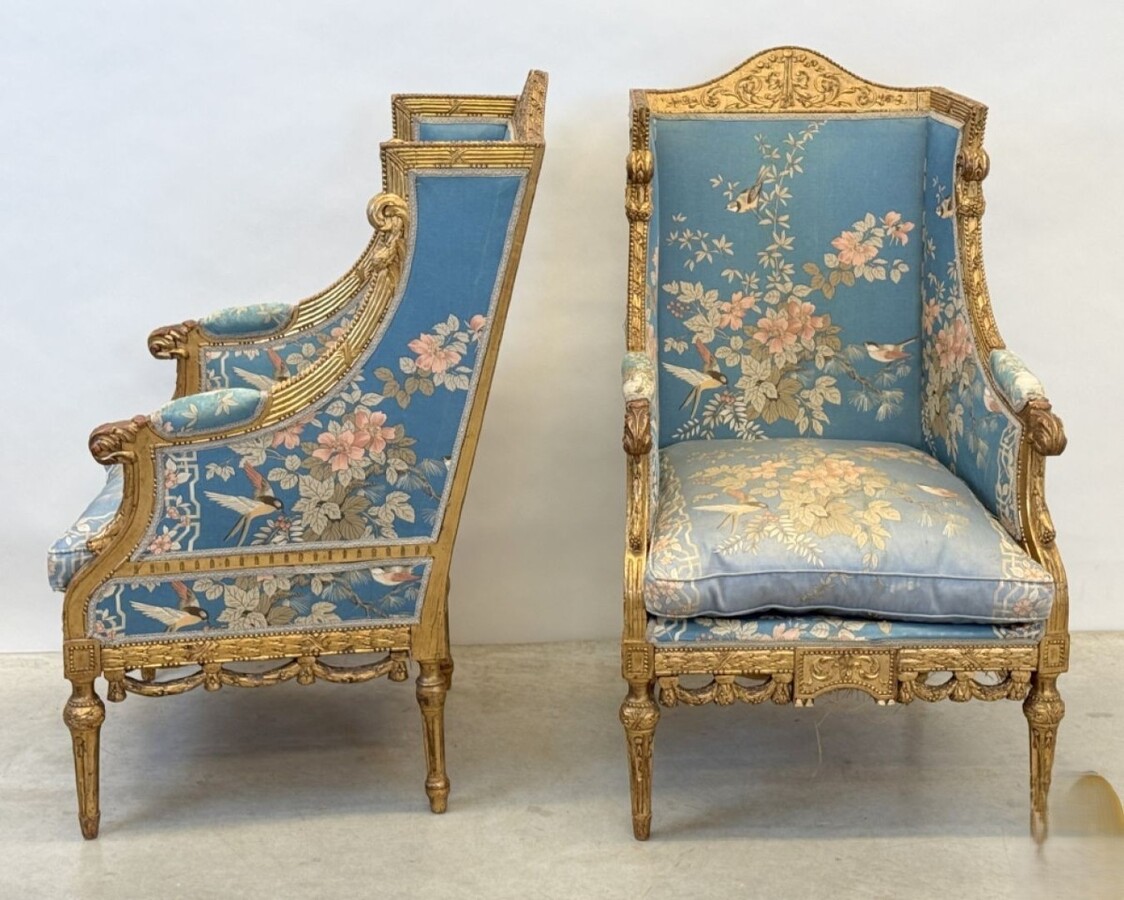Pair of giltwood bergères in the Louis Seize style 1900 Decorative bergères adorned with garlands and carved ornaments and upholstered in a beautiful blue fabric with bird and flower motifs. The seat of one of the armchairs needs restoring!