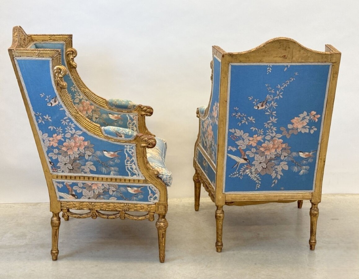Pair of giltwood bergères in the Louis Seize style 1900 Decorative bergères adorned with garlands and carved ornaments and upholstered in a beautiful blue fabric with bird and flower motifs. The seat of one of the armchairs needs restoring!