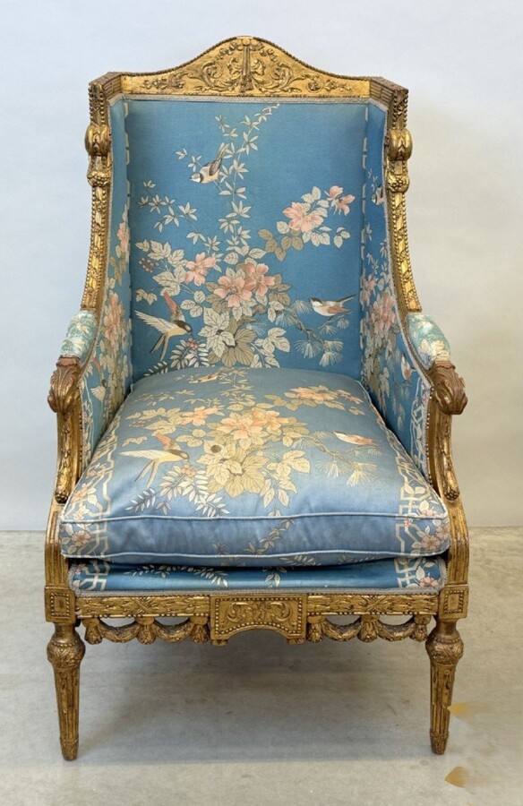 Pair of giltwood bergères in the Louis Seize style 1900 Decorative bergères adorned with garlands and carved ornaments and upholstered in a beautiful blue fabric with bird and flower motifs. The seat of one of the armchairs needs restoring!