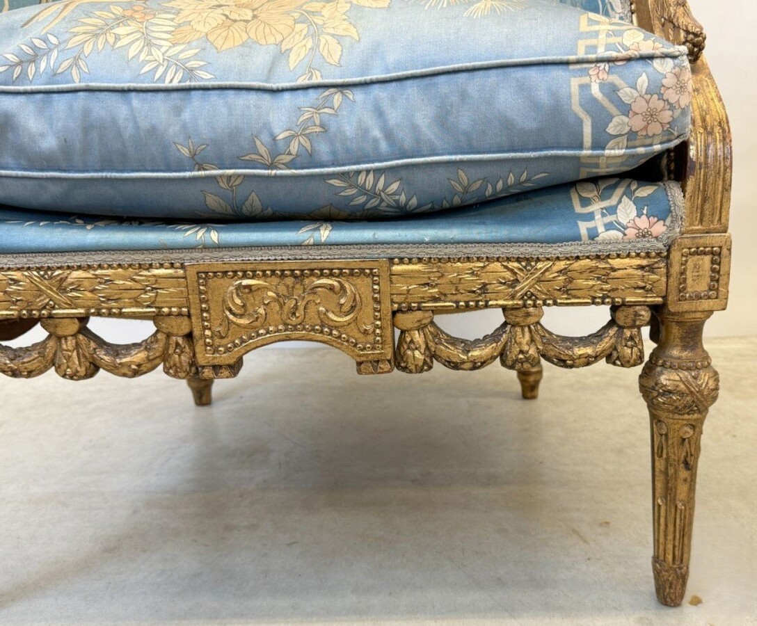 Pair of giltwood bergères in the Louis Seize style 1900 Decorative bergères adorned with garlands and carved ornaments and upholstered in a beautiful blue fabric with bird and flower motifs. The seat of one of the armchairs needs restoring!
