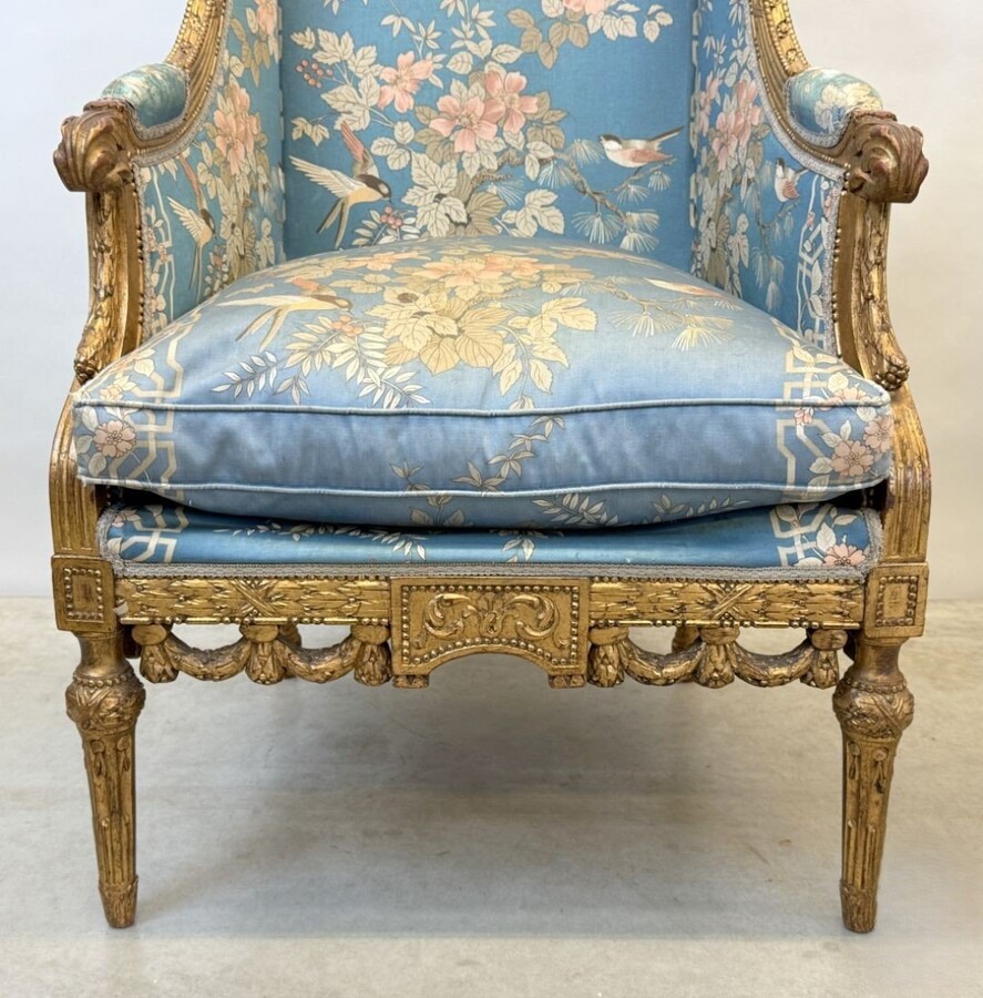 Pair of giltwood bergères in the Louis Seize style 1900 Decorative bergères adorned with garlands and carved ornaments and upholstered in a beautiful blue fabric with bird and flower motifs. The seat of one of the armchairs needs restoring!