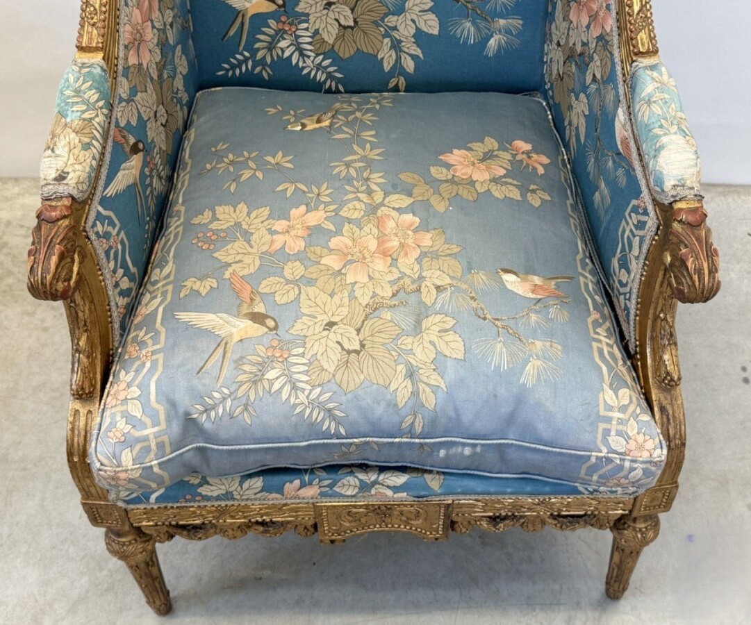 Pair of giltwood bergères in the Louis Seize style 1900 Decorative bergères adorned with garlands and carved ornaments and upholstered in a beautiful blue fabric with bird and flower motifs. The seat of one of the armchairs needs restoring!
