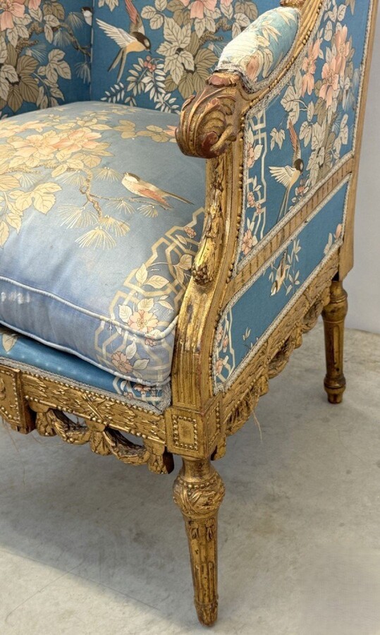 Pair of giltwood bergères in the Louis Seize style 1900 Decorative bergères adorned with garlands and carved ornaments and upholstered in a beautiful blue fabric with bird and flower motifs. The seat of one of the armchairs needs restoring!