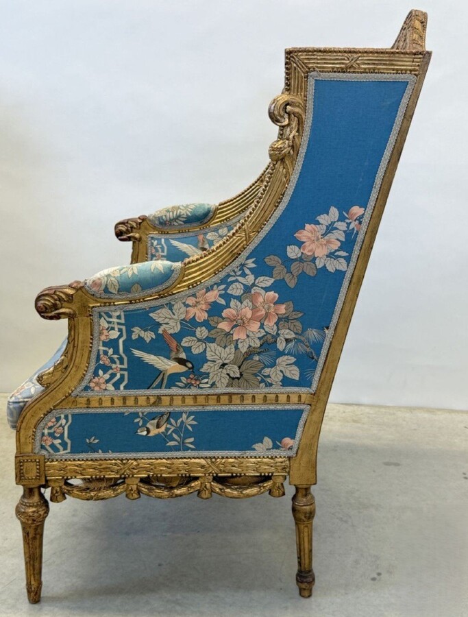 Pair of giltwood bergères in the Louis Seize style 1900 Decorative bergères adorned with garlands and carved ornaments and upholstered in a beautiful blue fabric with bird and flower motifs. The seat of one of the armchairs needs restoring!