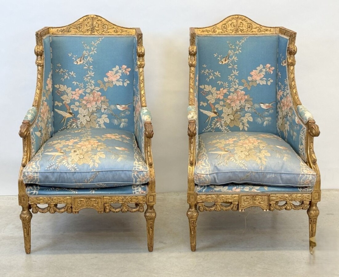 Pair of giltwood bergères in the Louis Seize style 1900 Decorative bergères adorned with garlands and carved ornaments and upholstered in a beautiful blue fabric with bird and flower motifs. The seat of one of the armchairs needs restoring!