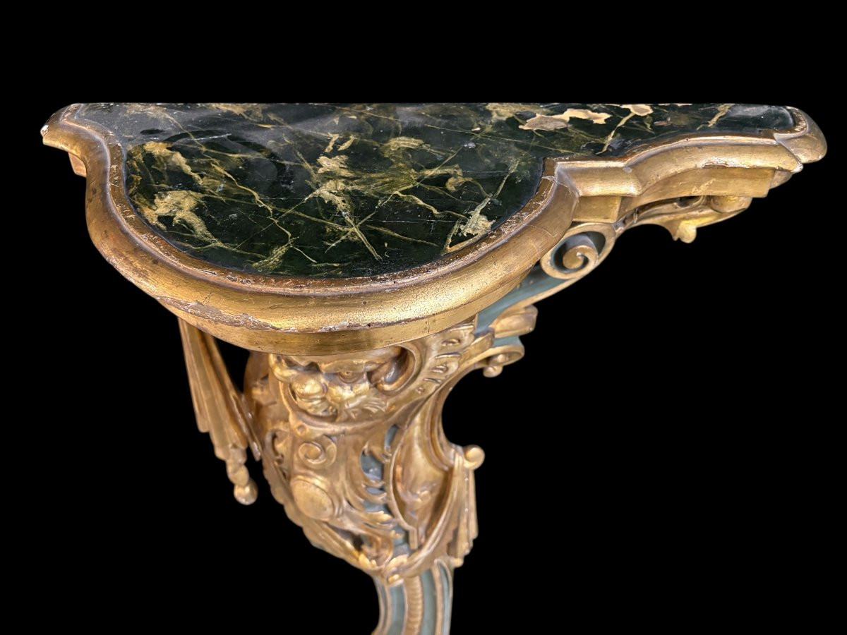 Pair of large, elegant 18th-century Italian wall consoles. Highly decorative consoles in gilded and patinated wood, adorned with a mythological head and decorated with drapery, volutes and ornaments. The top shelf is painted in faux marble. Italian,