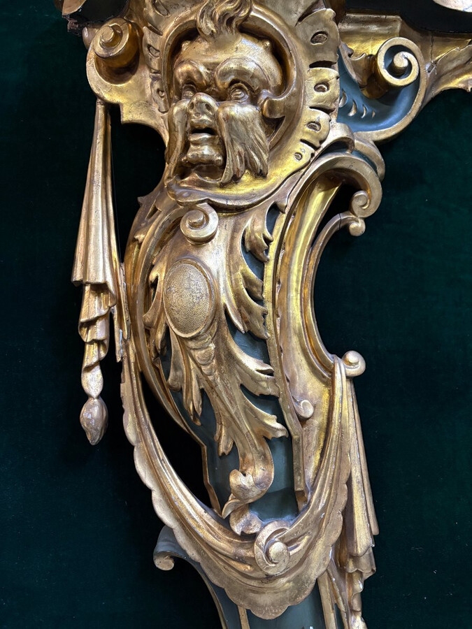 Pair of large, elegant 18th-century Italian wall consoles. Highly decorative consoles in gilded and patinated wood, adorned with a mythological head and decorated with drapery, volutes and ornaments. The top shelf is painted in faux marble. Italian,