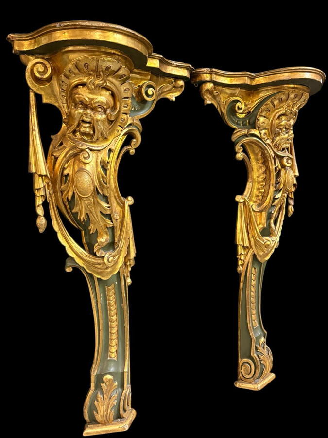 Pair of large, elegant 18th-century Italian wall consoles. Highly decorative consoles in gilded and patinated wood, adorned with a mythological head and decorated with drapery, volutes and ornaments. The top shelf is painted in faux marble. Italian,