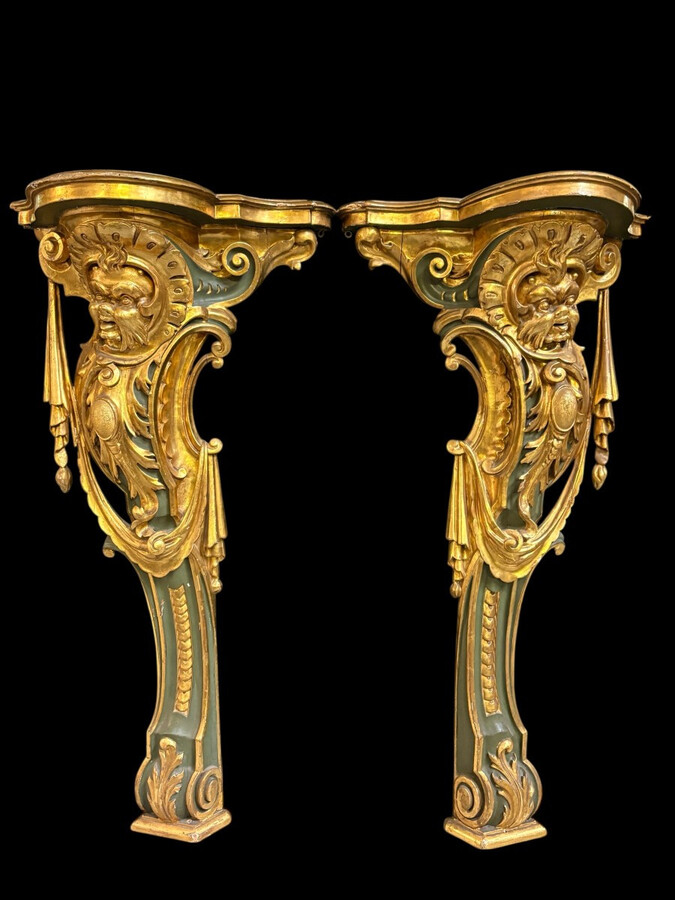 Pair of large, elegant 18th-century Italian wall consoles. Highly decorative consoles in gilded and patinated wood, adorned with a mythological head and decorated with drapery, volutes and ornaments. The top shelf is painted in faux marble. Italian,