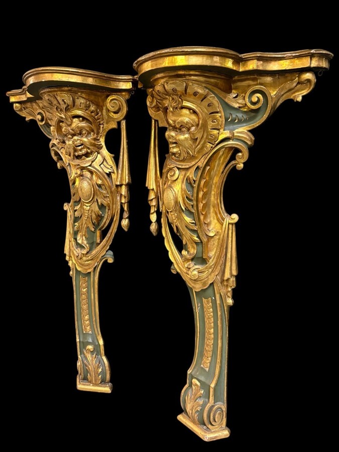 Pair of large, elegant 18th-century Italian wall consoles. Highly decorative consoles in gilded and patinated wood, adorned with a mythological head and decorated with drapery, volutes and ornaments. The top shelf is painted in faux marble. 