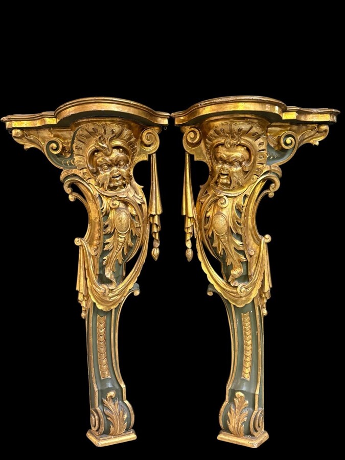 Pair of large, elegant 18th-century Italian wall consoles. Highly decorative consoles in gilded and patinated wood, adorned with a mythological head and decorated with drapery, volutes and ornaments. The top shelf is painted in faux marble. 