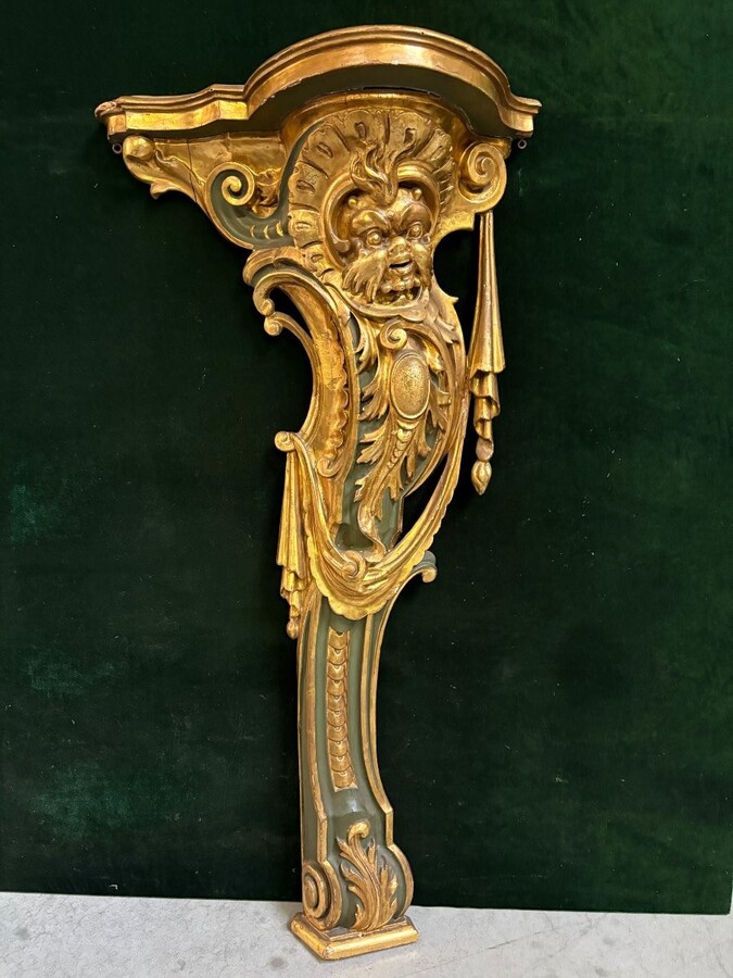 Pair of large, elegant 18th-century Italian wall consoles. Highly decorative consoles in gilded and patinated wood, adorned with a mythological head and decorated with drapery, volutes and ornaments. The top shelf is painted in faux marble. 