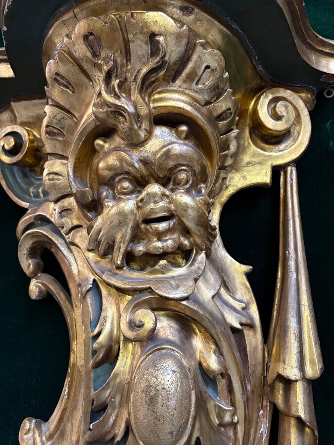 Pair of large, elegant 18th-century Italian wall consoles. Highly decorative consoles in gilded and patinated wood, adorned with a mythological head and decorated with drapery, volutes and ornaments. The top shelf is painted in faux marble. 