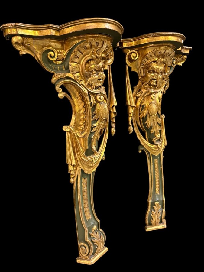 Pair of large, elegant 18th-century Italian wall consoles. Highly decorative consoles in gilded and patinated wood, adorned with a mythological head and decorated with drapery, volutes and ornaments. The top shelf is painted in faux marble. 