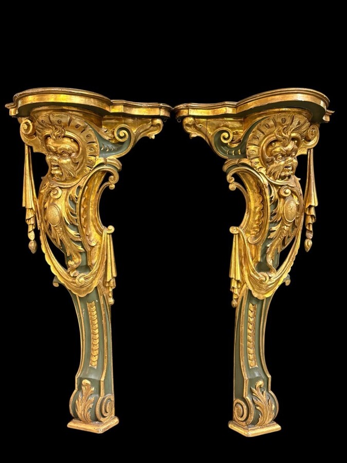 Pair of large, elegant 18th-century Italian wall consoles. Highly decorative consoles in gilded and patinated wood, adorned with a mythological head and decorated with drapery, volutes and ornaments. The top shelf is painted in faux marble.