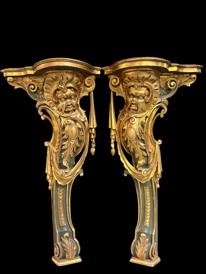 Pair of large, elegant 18th-century Italian wall consoles. Highly decorative consoles in gilded and patinated wood, adorned with a mythological head and decorated with drapery, volutes and ornaments. The top shelf is painted in faux marble.