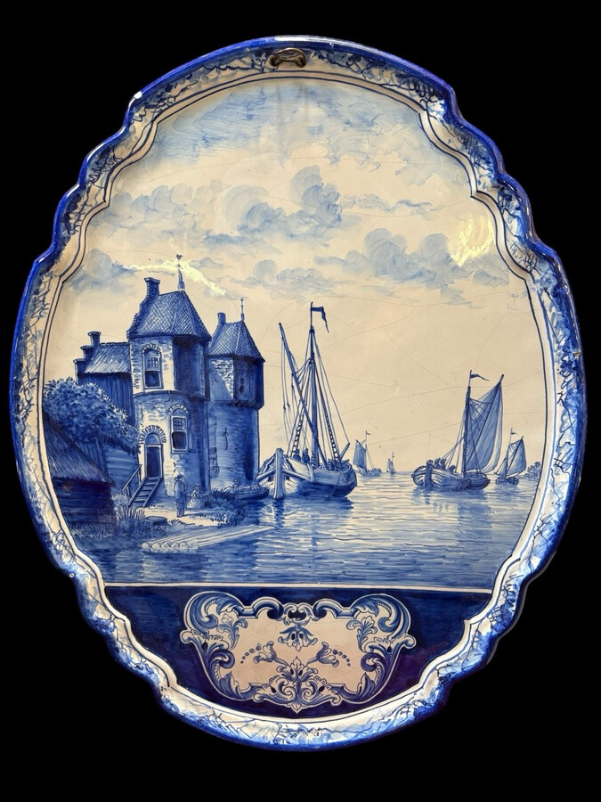 Pair of large Makkum earthenware wall plates Highly decorative blue and white earthenware wall plates depicting Dutch landscapes with windmills, water, boats, houses and animals. Fitted with a hanging loop and marked on the back.