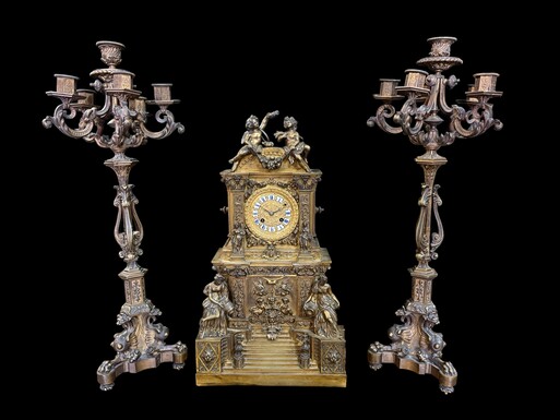 Romantic Napoleon III-style bronze mantelpiece set A mantelpiece set comprising a clock adorned with angels, figures, decorative motifs and a building with a staircase, as well as a pair of candlesticks richly decorated with mythological creatures. 