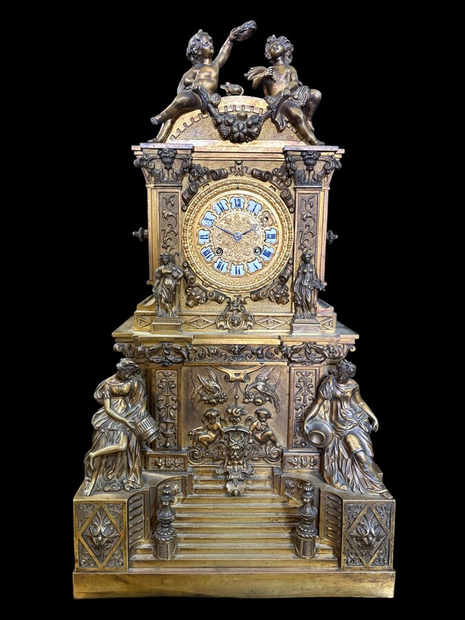 Romantic Napoleon III-style bronze mantelpiece set A mantelpiece set comprising a clock adorned with angels, figures, decorative motifs and a building with a staircase, as well as a pair of candlesticks richly decorated with mythological creatures. 