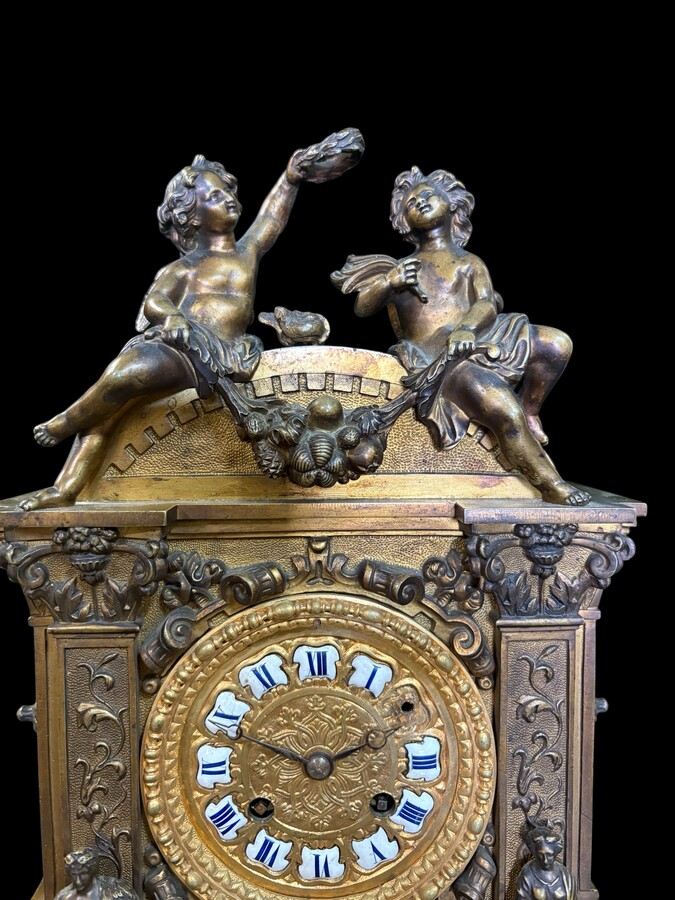 Romantic Napoleon III-style bronze mantelpiece set A mantelpiece set comprising a clock adorned with angels, figures, decorative motifs and a building with a staircase, as well as a pair of candlesticks richly decorated with mythological creatures. 