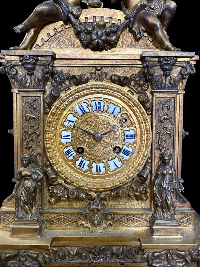 Romantic Napoleon III-style bronze mantelpiece set A mantelpiece set comprising a clock adorned with angels, figures, decorative motifs and a building with a staircase, as well as a pair of candlesticks richly decorated with mythological creatures. 