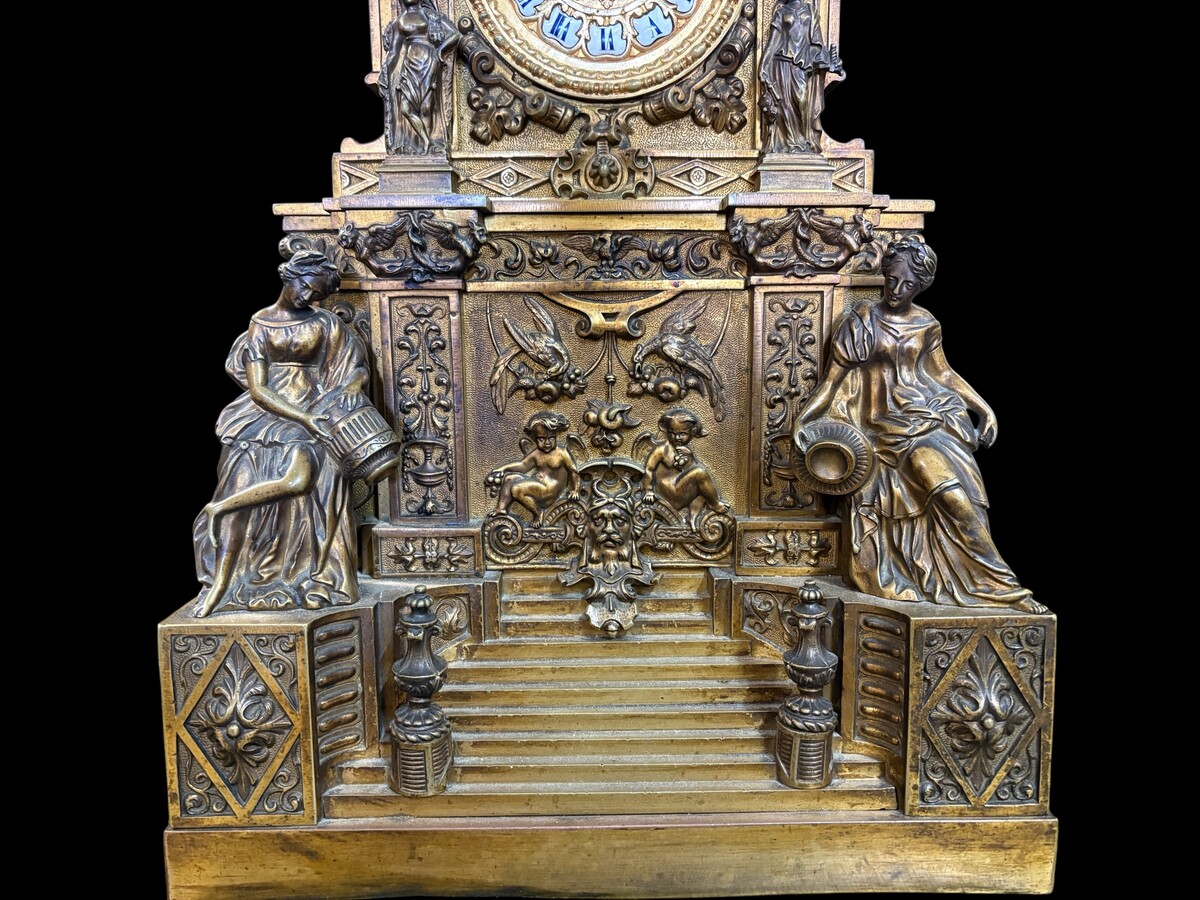 Romantic Napoleon III-style bronze mantelpiece set A mantelpiece set comprising a clock adorned with angels, figures, decorative motifs and a building with a staircase, as well as a pair of candlesticks richly decorated with mythological creatures. 