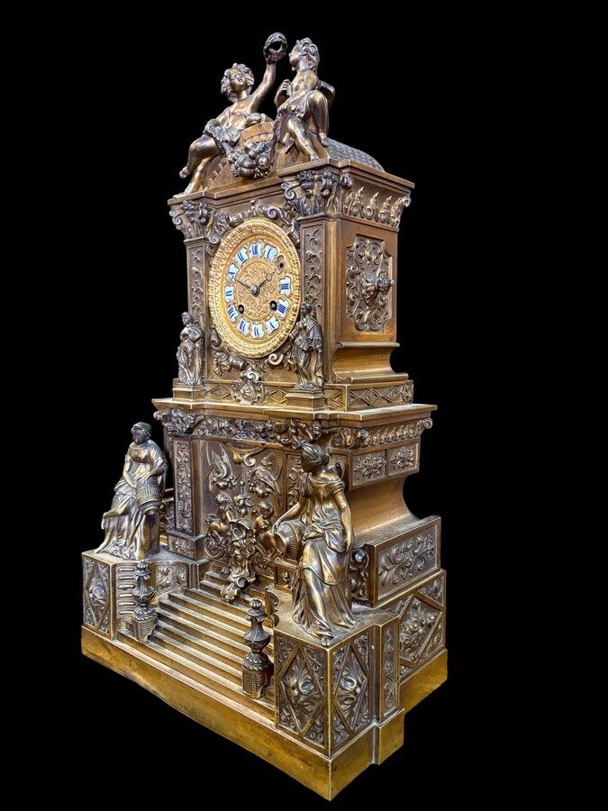 Romantic Napoleon III-style bronze mantelpiece set A mantelpiece set comprising a clock adorned with angels, figures, decorative motifs and a building with a staircase, as well as a pair of candlesticks richly decorated with mythological creatures. 