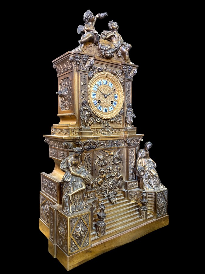 Romantic Napoleon III-style bronze mantelpiece set A mantelpiece set comprising a clock adorned with angels, figures, decorative motifs and a building with a staircase, as well as a pair of candlesticks richly decorated with mythological creatures. 