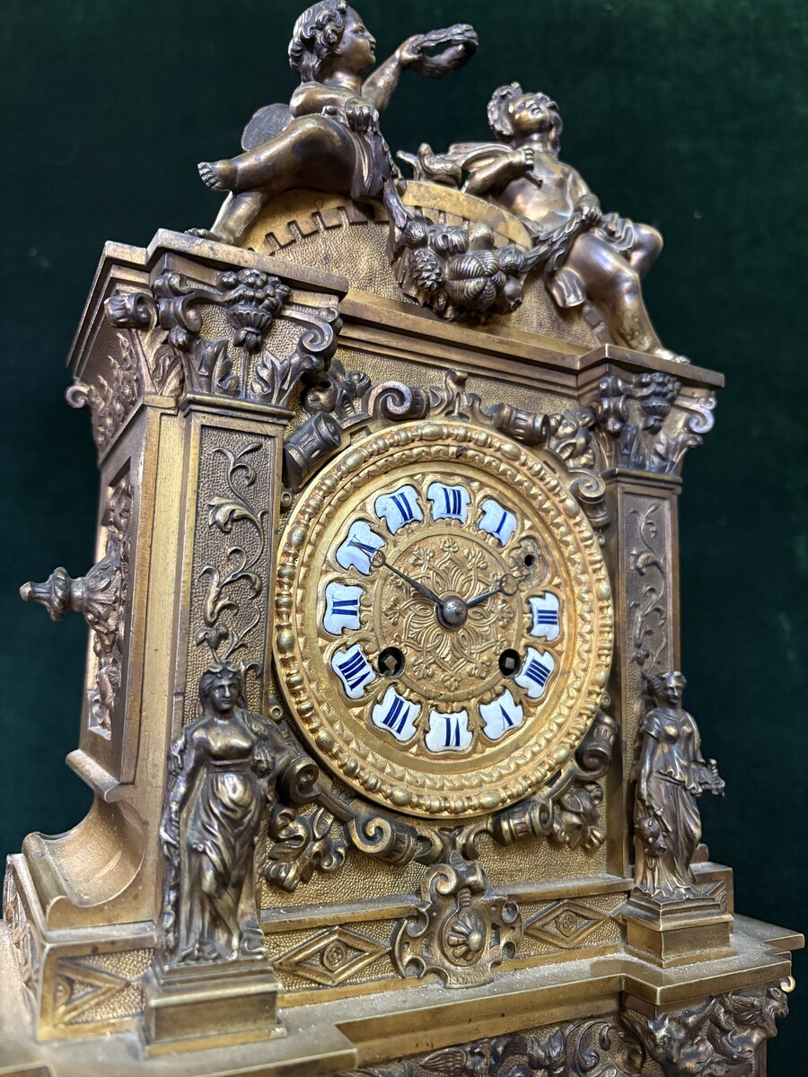 Romantic Napoleon III-style bronze mantelpiece set A mantelpiece set comprising a clock adorned with angels, figures, decorative motifs and a building with a staircase, as well as a pair of candlesticks richly decorated with mythological creatures. 