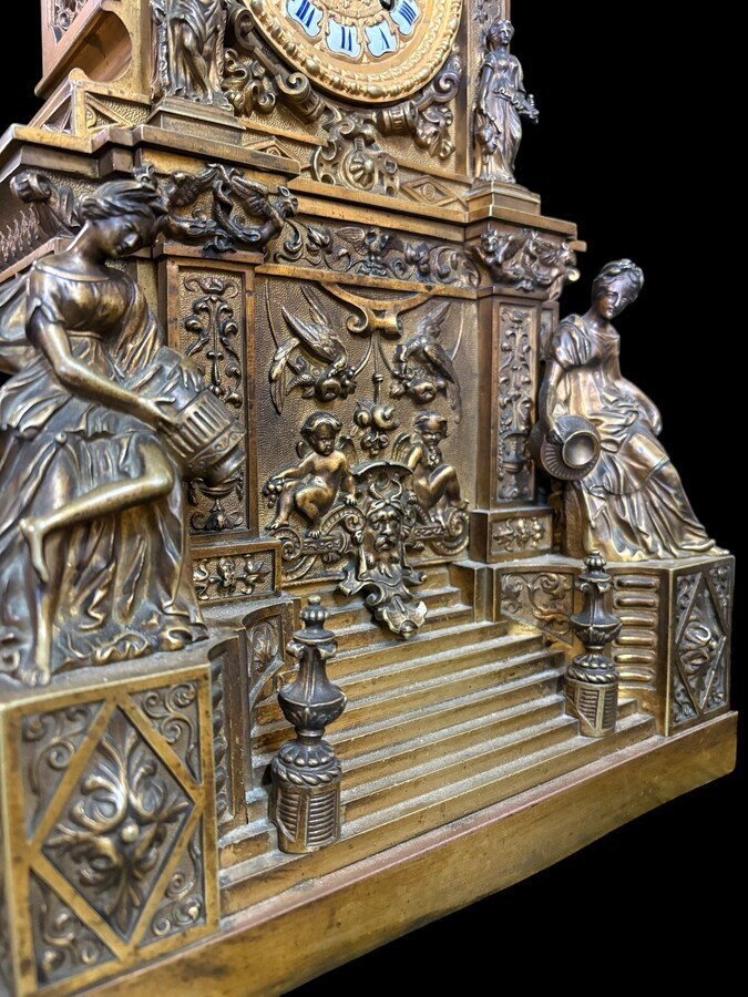 Romantic Napoleon III-style bronze mantelpiece set A mantelpiece set comprising a clock adorned with angels, figures, decorative motifs and a building with a staircase, as well as a pair of candlesticks richly decorated with mythological creatures. 