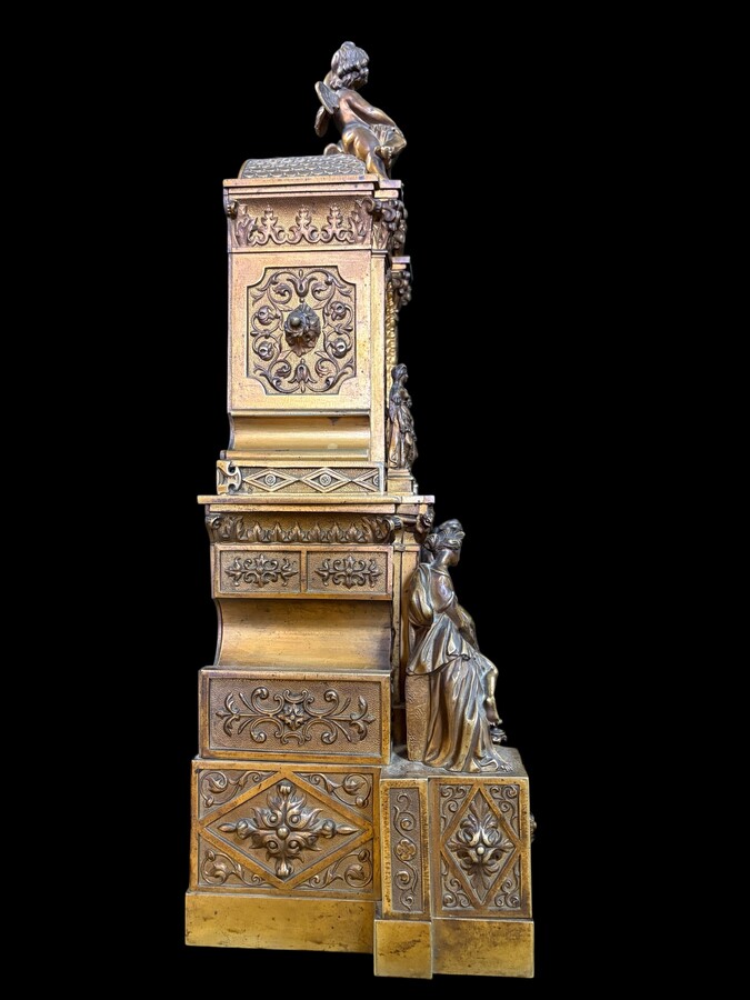 Romantic Napoleon III-style bronze mantelpiece set A mantelpiece set comprising a clock adorned with angels, figures, decorative motifs and a building with a staircase, as well as a pair of candlesticks richly decorated with mythological creatures. 